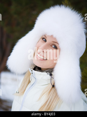 Portrait of fresh woman in white fur cap with ear-flaps and looking at camera with smile Stock Photo