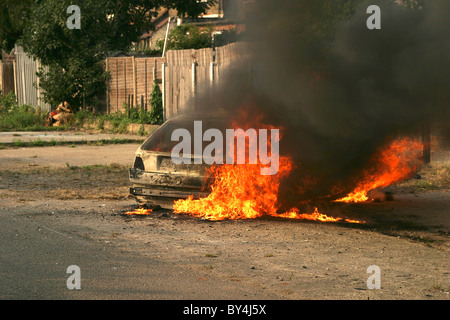 Car on fire next to house Stock Photo