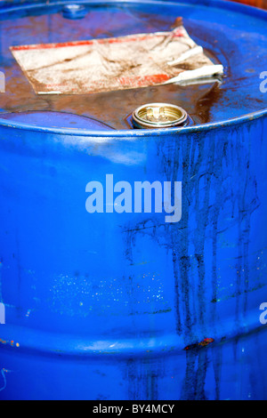 A dumped blue rusted corroded metal drum filled with unknown hazardous chemicals or toxic waste Stock Photo