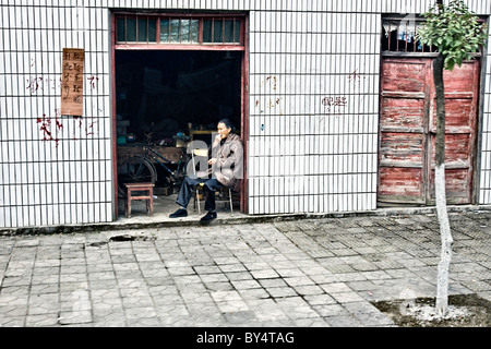 CHINA, YICHANG, SANDOUPING: Street scene of elderly woman eating a snack in the doorway of her shop. Stock Photo