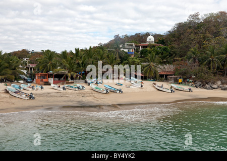 azure water laps golden sand with fishing boats drawn up on palm fringed beach at evening Puerto Angel Oaxaca State Mexico Stock Photo