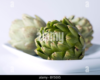 3 Artichokes sitting on a white platter Stock Photo