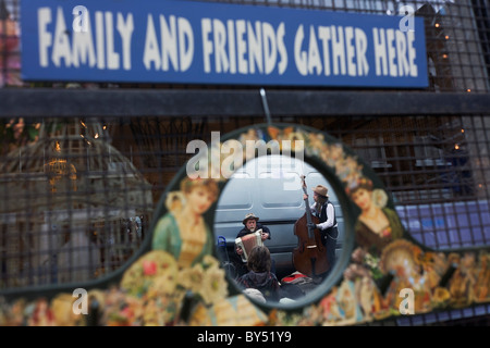 Street musicians play in Columbia Street market, seen through a shop's mirror where friends and family may gather. Stock Photo