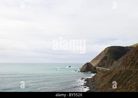 Waves crash against the rocky coast in Big Sur with Big Creek Bridge along California's Pacific Coast Highway, California, USA. Stock Photo