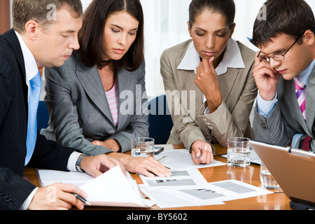 Photo of business group sitting at the table and watching at documents on it with pensive expression Stock Photo