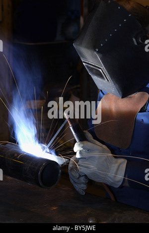 A man arc welding. Sparks are flying through the air, and smoke is being drawn out the exhaust system. Stock Photo