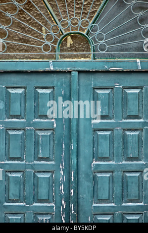 Weathered blue wooden gate with vintage ornamental sun pattern metalwork. Stock Photo