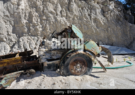 Rusty vintage car and discarded machinery half buried in the sand at gravel quarry. Stock Photo