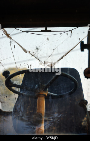 Steering wheel and driver cabin of industrial machinery. Light reflections on broken windscreen glass. Stock Photo