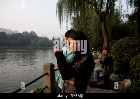 Teenage girls taking photograph at lake in Luxon Park, Shanghai, China Stock Photo