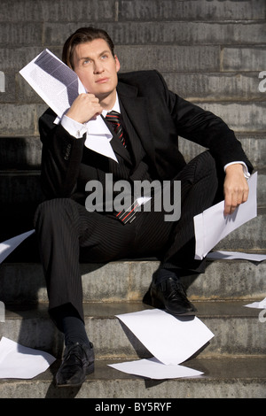 Portrait of depressed manager sitting with papers in hands and around him while looking slightly upwards Stock Photo