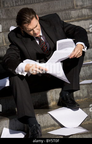 Photo of man reading documents with pensive expression while sitting on staircase Stock Photo
