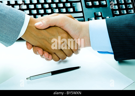 Image of two business people’s handshake after making an agreement on the background of keyboard, pen, paper Stock Photo
