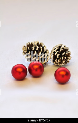 Three red Christmas baubles and two pine cones on a white background. UK December 2010 Stock Photo