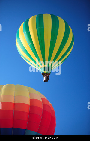 2 colorful hot air balloons floating lazily away on a vibrant blue sky. Stock Photo