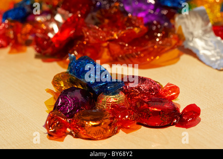 pile wrapped up quality street chocolate sweets with pile of empty colourful wrappers in the background Stock Photo