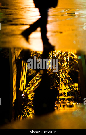 PARIS, France — A passerby walks past a puddle reflecting some of the detail of the Eiffel Tower at night. Stock Photo