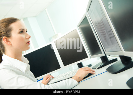 Profile of confident female looking at computer screen while touching mouse and pressing key in workshop Stock Photo