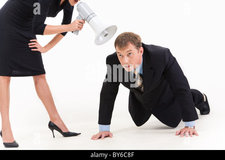 Image of businessman in suit doing physical exercise while standing woman shouting at him through loudspeaker Stock Photo