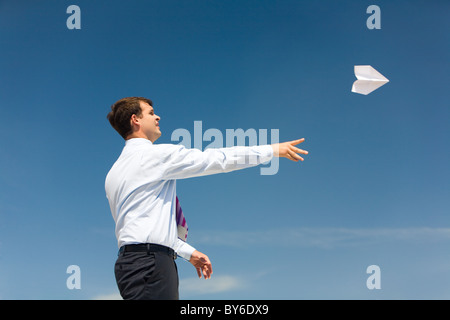 Conceptual photo of businessman standing with his arm stretched after launching paper aeroplane into bright sky Stock Photo