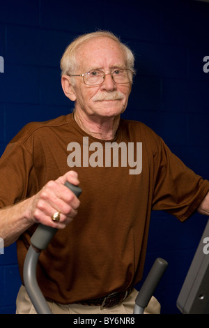 Happy senior man works out on an elliptical machine at the gym. Stock Photo