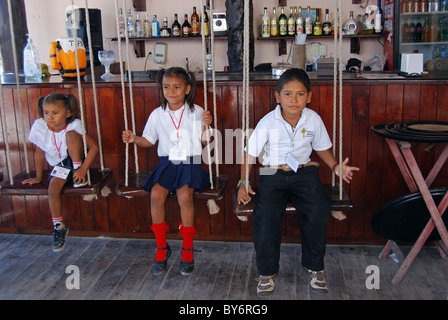 Mexican children sitting on swings at a bar, Costa Maya, South Eastern Region, Mexico, Caribbean. Stock Photo