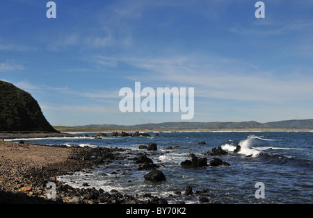 Blue sky inland view of a white breaker on basalt beach below cliffs, Mar Brava, Cocotue Bay, Pacifc Coast, Chiloe Island, Chile Stock Photo