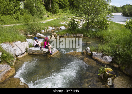 Two girls sitting on rocks in river Isar, Isar renaturation, fish-ladder near Bad Toelz, Isar Cycle Route, Upper Bavaria, German Stock Photo