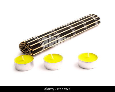 Black bamboo mat with three small yellow candles on white background. Stock Photo