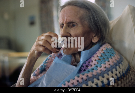 An elderly woman patient wearing a crocheted shawl sitting in bed drinking in a  hospital ward in Wales UK Great Britain   KATHY DEWITT Stock Photo