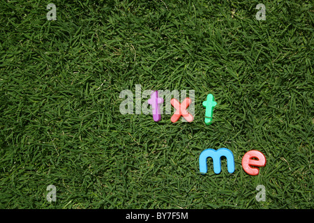 The words 'txt me' spelled out in colourful plastic letters, on green grass, taken from a low angle Stock Photo