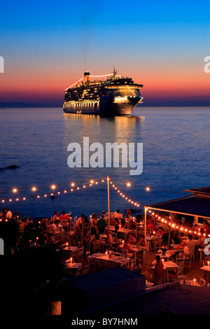 A seaside restaurant and a cruise ship, somewhere between 'Little Venice' and the windmills in the Hora of Mykonos, Greece Stock Photo