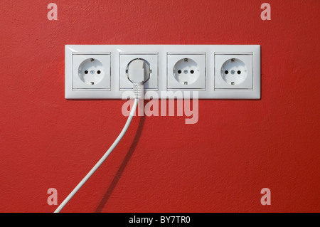 Electrical outlets, cable and electric plug on red textured wall Stock Photo