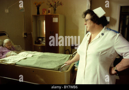 A staff nurse checking on an elderly senior woman female patient lying in her bed in Bronglais Hospital ward in the 1980s Aberystwyth Wales UK   KATHY DEWITT Stock Photo