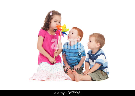 Three kids blowing toy windmill. Isolated on white. Stock Photo