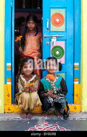 Young indian girls holding orange gerbera flowers in the doorway of a colourful home. Andhra Pradesh, India Stock Photo