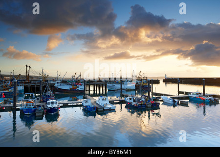 Dramatic rain clouds catching the light of dawn pass over and reflect in the calm waters of Newlyn Harbour Stock Photo