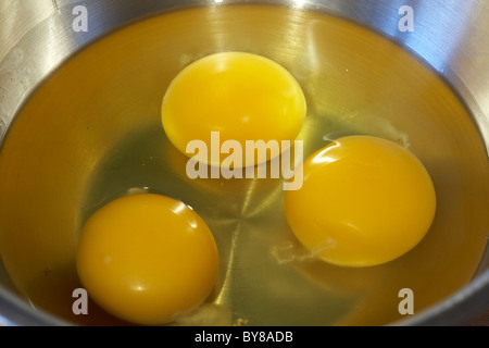 three eggs broken in a metal mixing bowl Stock Photo