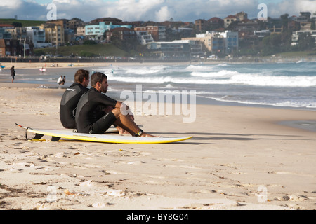 Two surfers sitting and watching the waves at Bondi Beach in Sydney, Australia Stock Photo