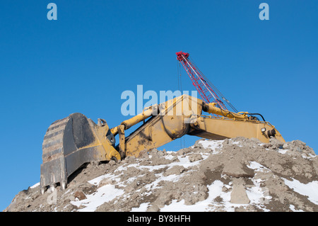 The arm and bucket of a hydraulic excavator on top of a pile of earth in winter with a crane in the background. Stock Photo