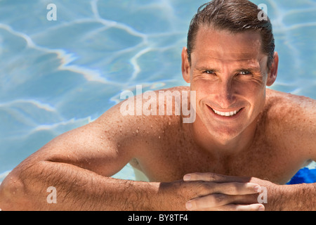 Close up portrait of a handsome and happy mid aged man relaxing resting on his hands at the side of a sun bathed swimming pool Stock Photo