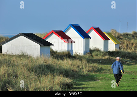 Woman walking past colourful beach cabins in the dunes at Gouville-sur-Mer, Normandy, France