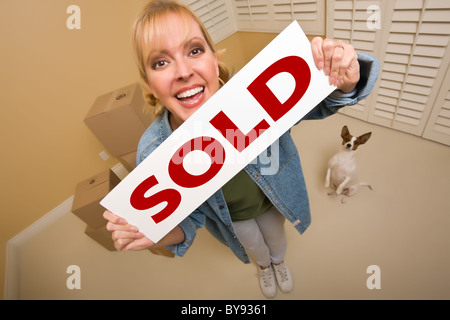 Excited Woman and Doggy with Sold Real Estate Sign Near Moving Boxes in Empty Room Taken with Extreme Wide Angle Lens. Stock Photo