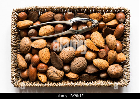 Mixed edible nuts in a basket with a metal nutcracker Stock Photo