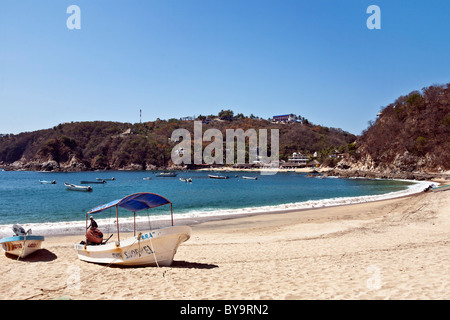 beautiful stretch of deserted sand beach with beached boats rings azure blue crescent of Puerto Angel bay Oaxaca State Mexico Stock Photo