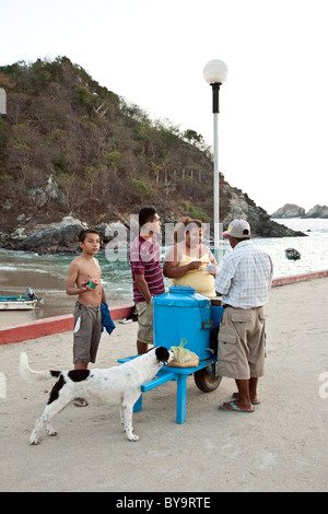 ice cream vendor serving customers in evening from bright blue hand made cart on pier at Puerto Angel Oaxaca State Mexico Stock Photo