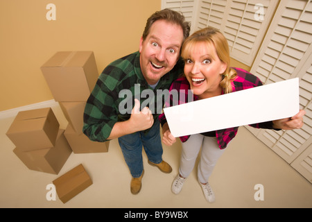 Goofy Thumbs Up Couple Holding Blank Sign in Room with Packed Cardboard Boxes. Stock Photo