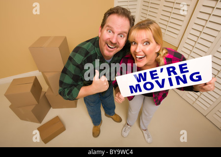 Goofy Thumbs Up Couple Holding We're Moving Sign in Room with Packed Cardboard Boxes. Stock Photo