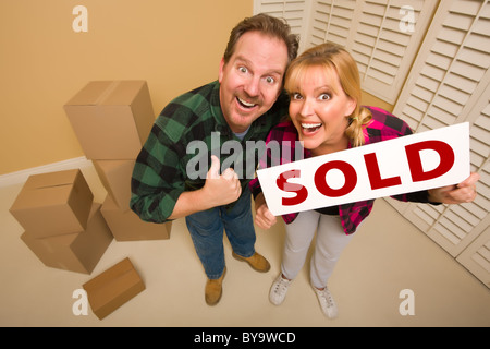 Goofy Thumbs Up Couple Holding Sold Sign in Room with Packed Cardboard Boxes. Stock Photo