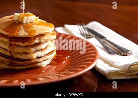 Maple syrup being poured over pancakes and butter. Stock Photo